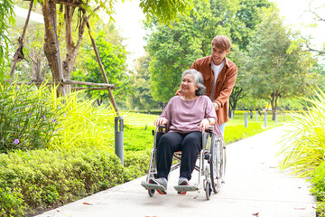 A son takes care of an elderly mother in a wheelchair taking her for a walk in an outdoor park. Asian family concept