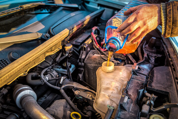 Auto mechanic hands filling pre-mixed super long life coolant antifreeze fluid in car radiator fill hole
