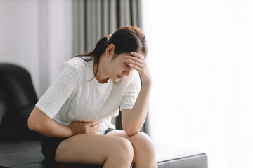 Young asian woman stomach ache sitting on bed at home, Health problem Inflammation in body, Period...