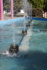 Fuente en el parque urbano de la ciudad con chorros de agua verticales salpicando la superficie,...
