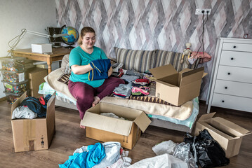 Overweight woman sorting clothes from wardrobe, spring cleaning, donating clothes, a mess in the...