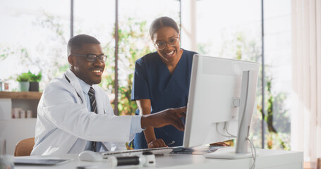 Health Care Medical Hospital. Happy African American Nurse and Black Doctor Having a Casual Conversation, Using Desktop Computer, Laughing and Smiling During a Break at Work