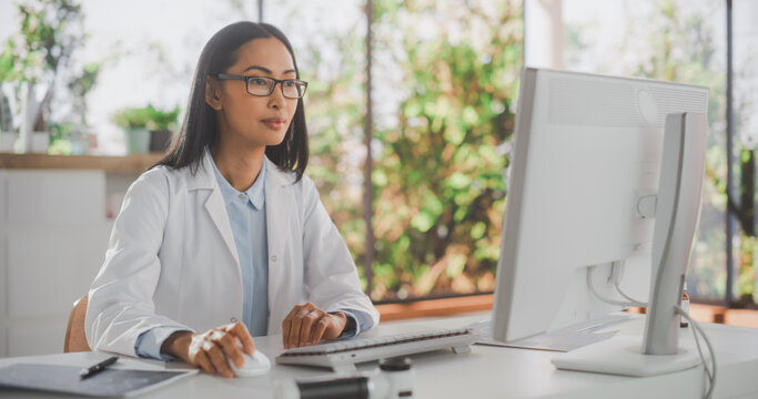 Portrait of an Asian Medical Health Care Professional Working on Desktop Computer in Hospital Office. Female Clinic Physician Appointing Prescriptions Online, Updating Electronic Health Records