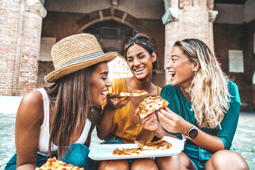 Three young female friends eating pizza sitting outside - Multiracial women enjoying street food in...