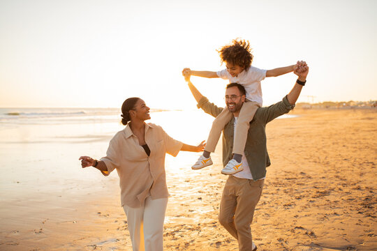 Joyful family beach day. Happy family having fun, father carrying son on shoulders and walking together along seaside