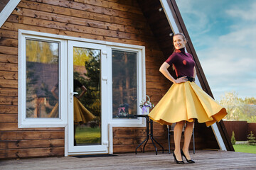 Cheerful woman in long waving skirt and pullover dancing on terrace of a-frame cabin