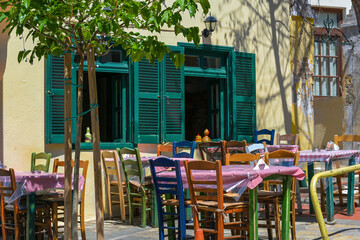 Fototapeta na wymiar Rustic Mediterranean tavern or casual street restaurant with different painted wooden chairs at the tables in front of the windows of a traditional house in the old town Thessaloniki, Greece