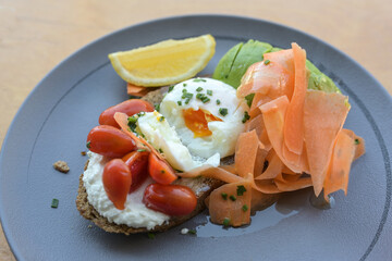 Healthy breakfast or lunch sandwich with rye bread, cream cheese, tomatoes, boiled egg, avocado and thinly sliced carrots served on a blue plate, selected focus