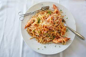 Spaghetti with shrimps in tomato sauce garnished with herbs and parmesan cheese on a plate and a white tablecloth, high angle view from above, copy space, selected focus