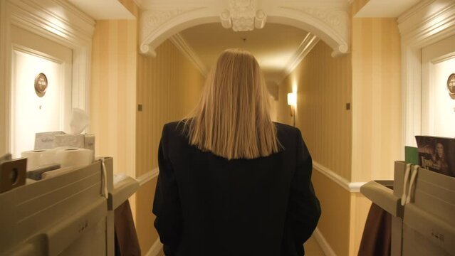 Back view of formally dressed in black suit female girl in Luxury modern room corridor. Woman arriving on business trip. Modern lobby interior in hotel. High quality 4k footage