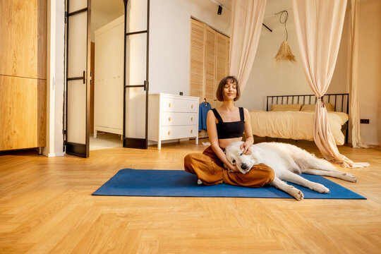 Young woman cares her cute dog, hugs together while doing yoga at home. Concept of dog therapy and mental health