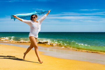 Beautiful woman walking on sunny beach holding shawl