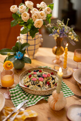 Fototapeta na wymiar Tasty pasta with spinach and berries decorated with edible flowers on a plate for sharing at beautifuly served dining table
