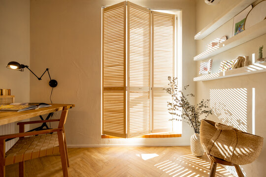 Interior view of workspace with wooden table and chair near the window with shutters in stylish studio apartement