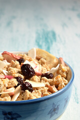 Bowl of delicious breakfast muesli with dried coconut, banana, apple, cranberries, raisins on a shabby chic wooden background. 
