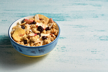 Bowl of delicious breakfast muesli with dried coconut, banana, apple, cranberries, raisins on a shabby chic wooden background. 
