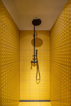 Shower cabin made with yellow tactile tiles with a black faucet