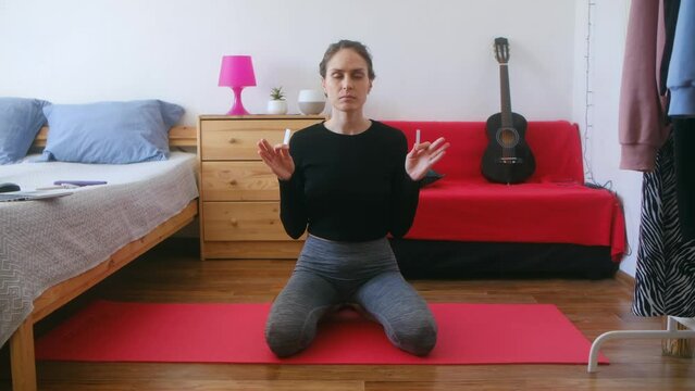 Pretty brunette young woman doing yogic practices at home modern interior. Girl with closed eyes meditating with mineral selenite in your hands.