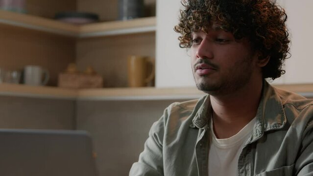 Tired frustrated overworked ill sick Indian man freelancer Arabian guy businessman suffer with headache tooth pain teeth ache migraine discomfort working with laptop online problem from home kitchen