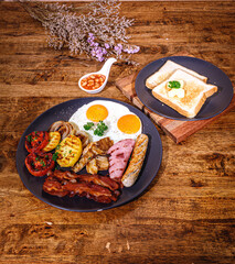 English Breakfast in cooking pan with fried eggs, sausages, bacon, beans, toasts on dark stone background copy space