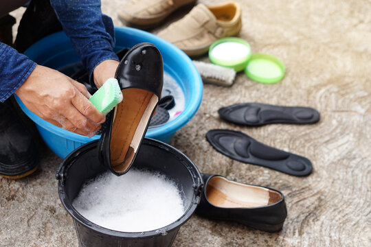 Closeup hands use brush to clean and wash black shoes in black bucket and blue bowl outdoor. Concept, take care, maintenance footwears from dirt and bad smell for using long time. Hygiene and sanitary
