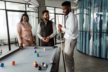 Young multiracial group of people in suits playing pool at office lobby