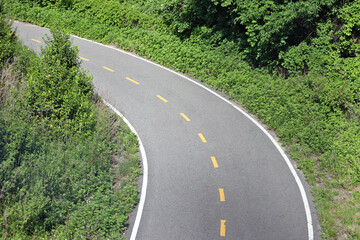 curved road with green trees and plants (smooth pavement bike lane with broken yellow centerline) turn curve paved path