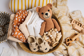 Basket with baby stuff and accessories for newborn. Gift basket with cotton clothes and muslin swaddle blanket, baby shoes, toys and cute teddy bear in beige colors.