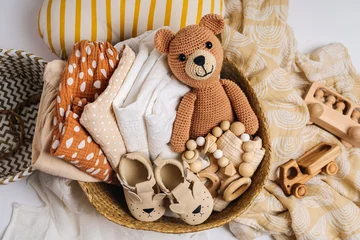 Fototapeten Basket with baby stuff and accessories for newborn. Gift basket with cotton clothes and muslin swaddle blanket, baby shoes, toys and cute teddy bear in beige colors. © igishevamaria