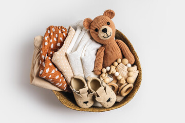 Basket with baby stuff and accessories for newborn. Gift basket with cotton clothes and muslin swaddle blanket, baby shoes, toys and cute teddy bear in beige colors. - obrazy, fototapety, plakaty