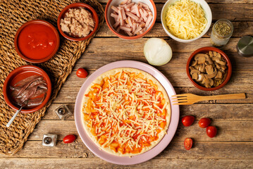 Pizza mold with tomato and mozzarella, next to the ingredients to prepare a pizza to taste, top view.