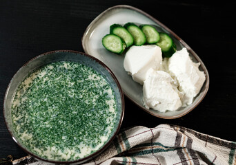 Okroshka, traditional Ukrainian and russian cold cucumber soup, served with sour cream and fresh cut cucumbers on black background