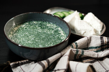 Okroshka, traditional Ukrainian and russian cold cucumber soup, served with sour cream and fresh cut cucumbers on black background
