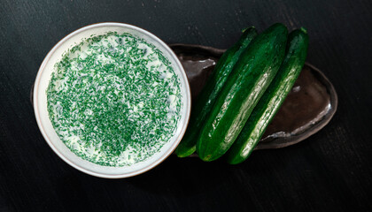 Okroshka, traditional Ukrainian and Russian cold cucumber soup, served with textile cloth and fresh cucumbers on wooden background