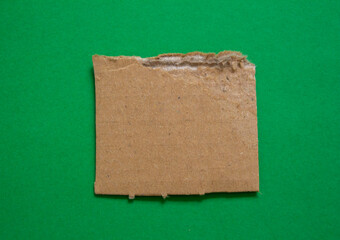 Ripped cardboard paper piece on green background with copy space.