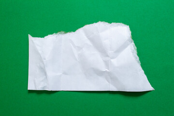 Crumpled piece of white paper isolated on a green background. Ripped paper.