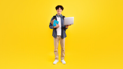 Positive Student Guy Holding Laptop And Textbooks Over Yellow Background