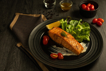 Grilled or fried salmon steak and green salad, lemon, tomato, sauce, side dish. Healthy traditional seafood with cooked fish