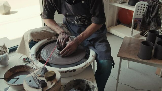 The potter works on the potter's wheel by the window. The process of making ceramic dishes from black clay.