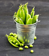 Fresh green peas in a small metal bucket on dark wooden background
