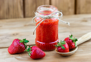 Fototapeta na wymiar Jar of strawberry mash with fresh strawberries in the spoon on wooden background