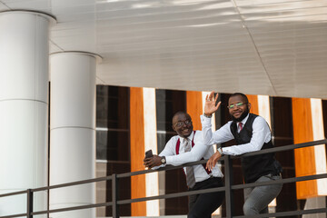 Portrait of two dark-skinned businessmen talking in the background of a modern building exterior. Friendly meeting outdoors