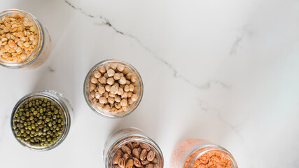 Legumes in glass jars top view on white background. Vegetable protein, healthy eating. Copy space