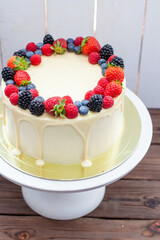 Cheesecake with fresh strawberry, raspberry, blueberry and blackberry, melted white chocolate on rustic wooden cakestand and background