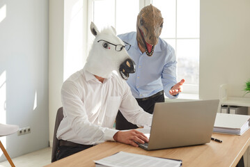 Funny animal people work in office. Two men in unusual disguise use laptop. Man wearing horse mask...
