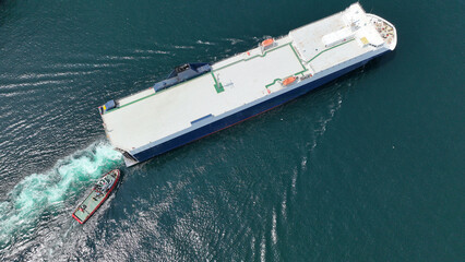 Aerial drone photo of large car carrier ro ro vessel guided by tug boats to dock to Mediterranean port