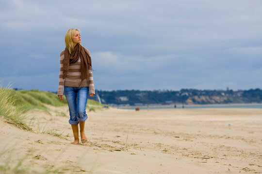 A beautiful young blond woman walks along a sandy beach