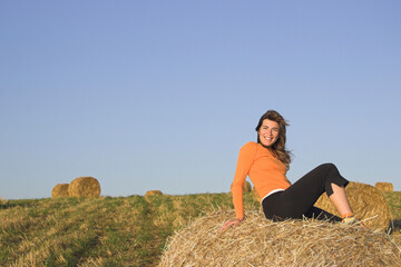 Naklejka na ściany i meble Beautiful woman in a field with hay bales