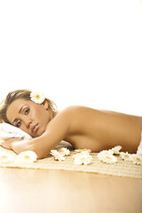 Obraz na płótnie Canvas Portrait of Fresh and Beautiful blond woman laying on bamboo mat around flowers and taking spa treatment