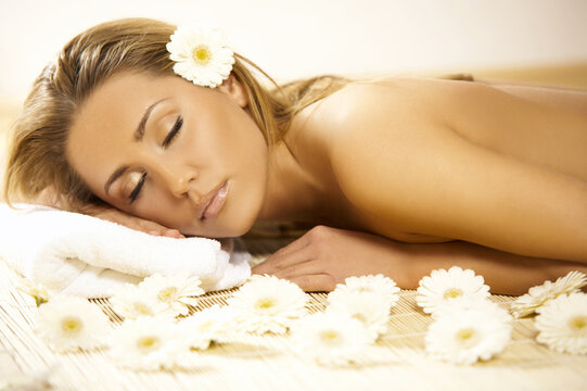 Portrait of Fresh and Beautiful blond woman laying on bamboo mat around flowers and taking spa treatment